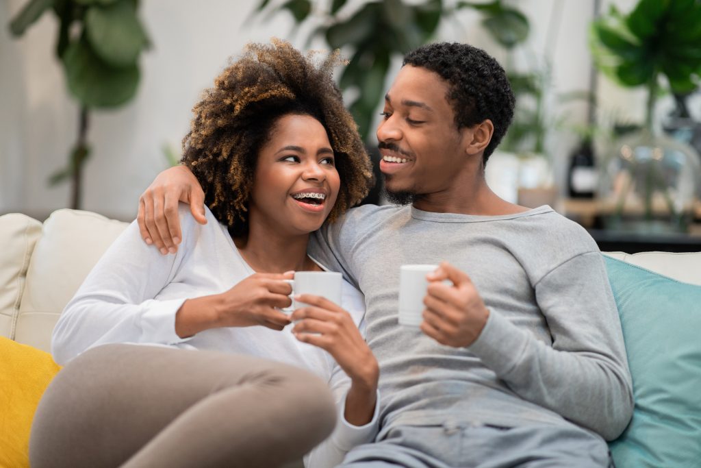 Cheerful black man and woman drinking coffee at home